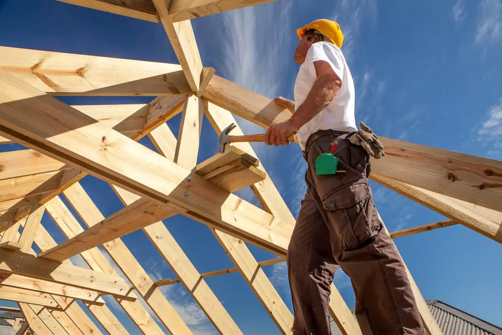 A man in yellow hard hat working on roof structure.